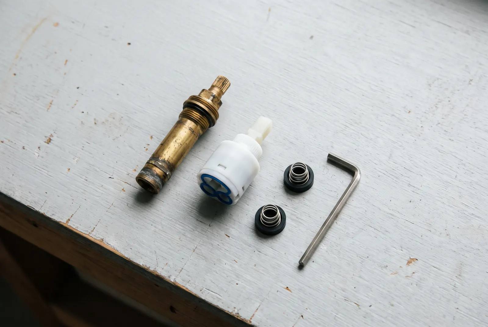 A brass faucet stem, a plastic cartridge, seats and springs and an Allen key laid out on a workbench A brass faucet stem, a plastic cartridge, seats and springs and an Allen key laid out on a workbench