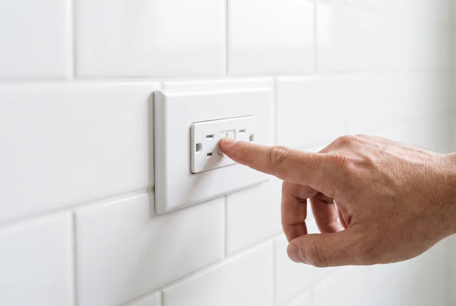 A finger pressing the reset button on a GFCI bathroom outlet
