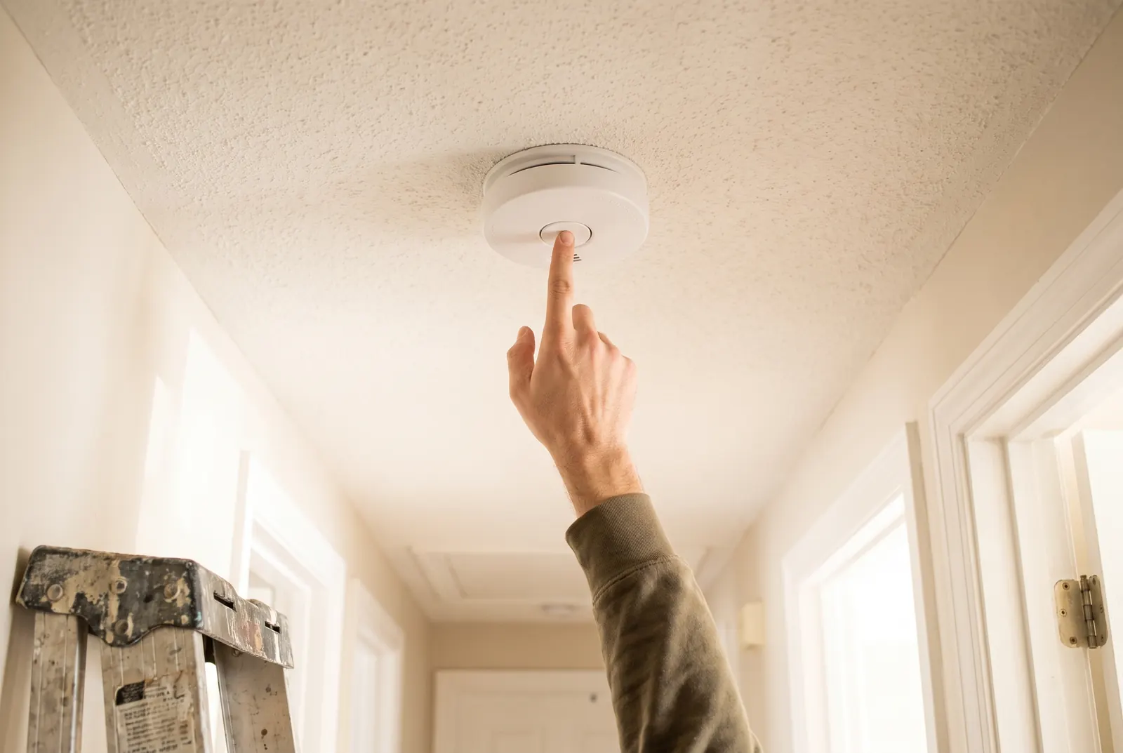 A hand reaching up to press the test button on a ceiling smoke alarm A hand reaching up to press the test button on a ceiling smoke alarm